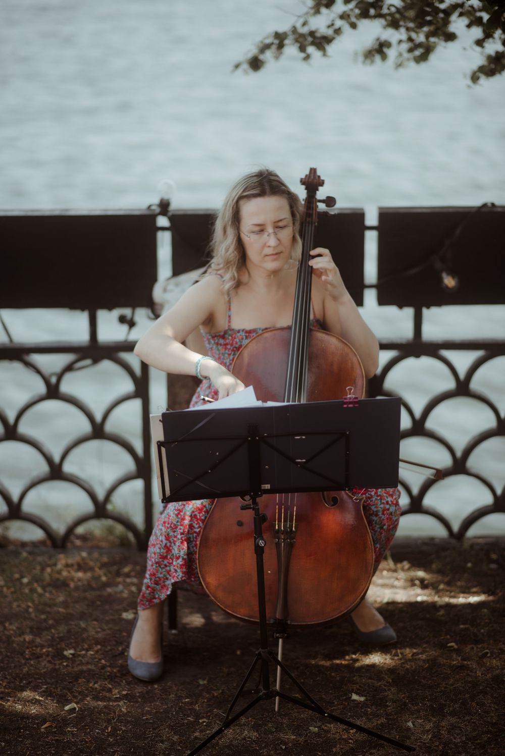 Musician performs on cello outdoors by waterfront during wedding celebration.