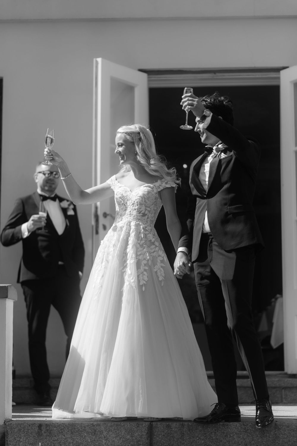 A celebratory moment captured in black and white as wedding party members raise their glasses outside.