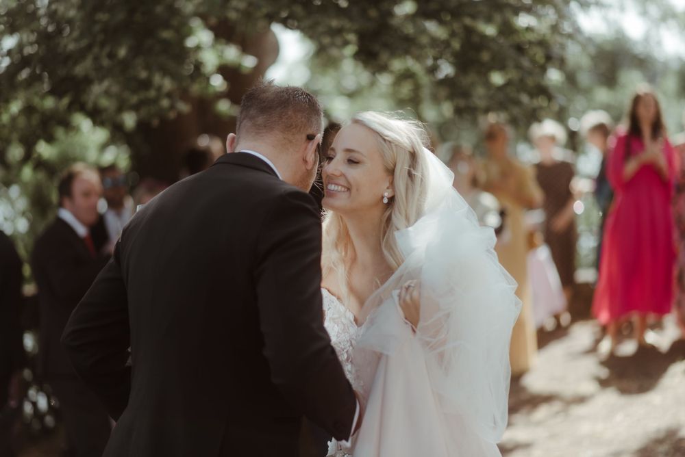 A romantic wedding moment captured in soft sunlight as guests look on.