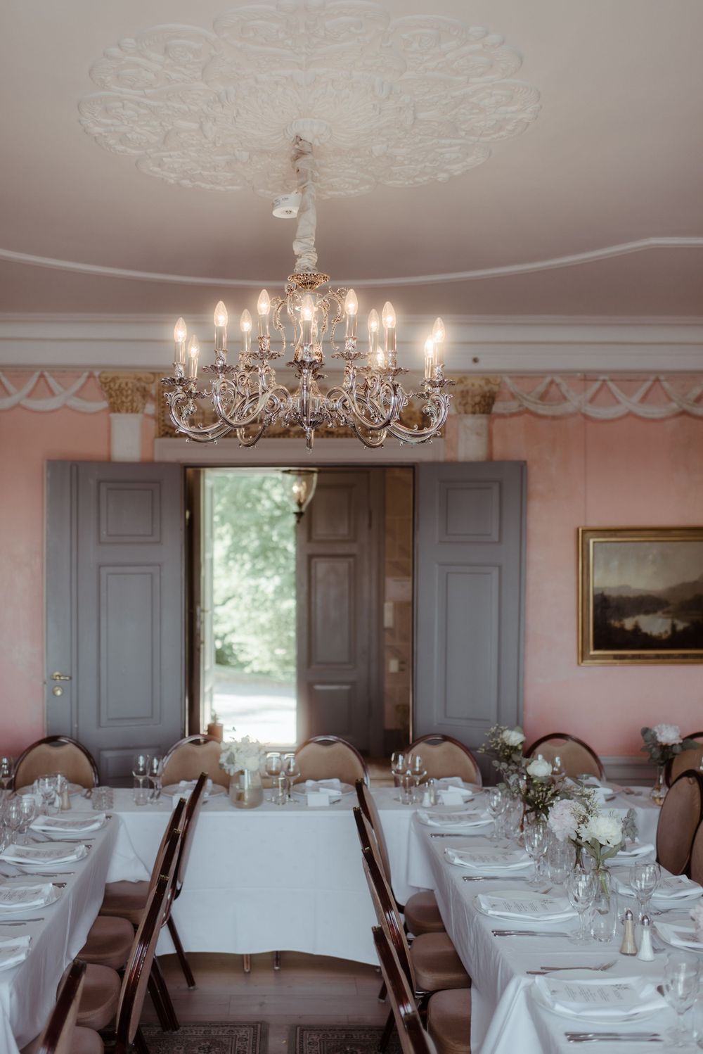 An elegant dining room with crystal chandelier and white-clothed tables set for a formal event.