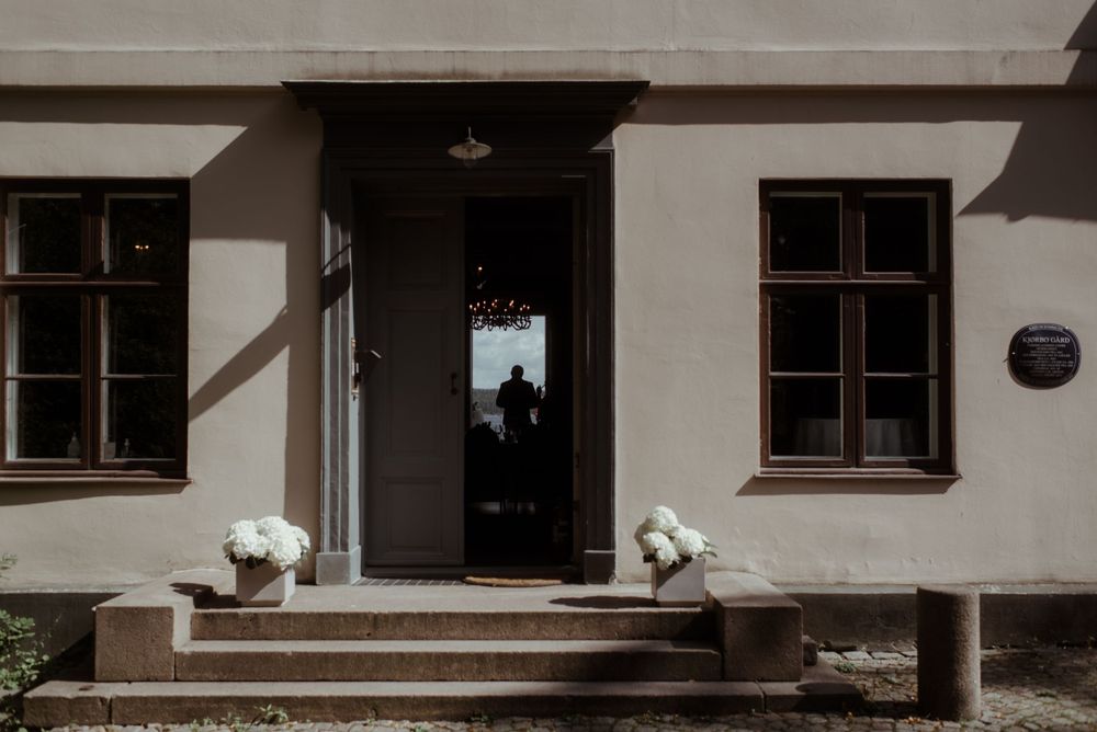 White building entrance with symmetrical windows and flower decorations on the front steps.