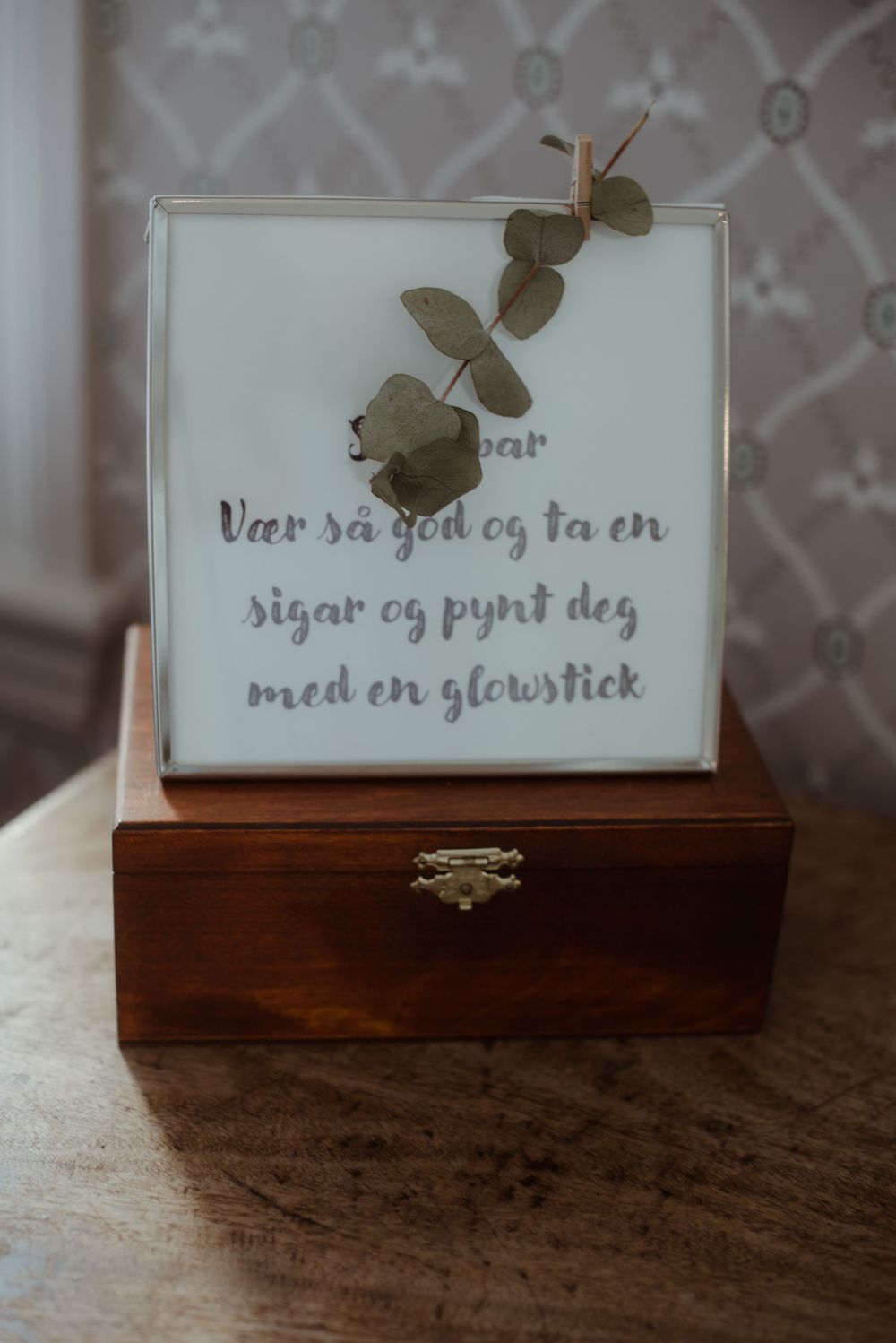 Wooden box with decorative text and eucalyptus sprig on white surface.