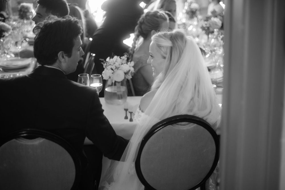Black and white photograph of an intimate wedding reception moment at a dining table.