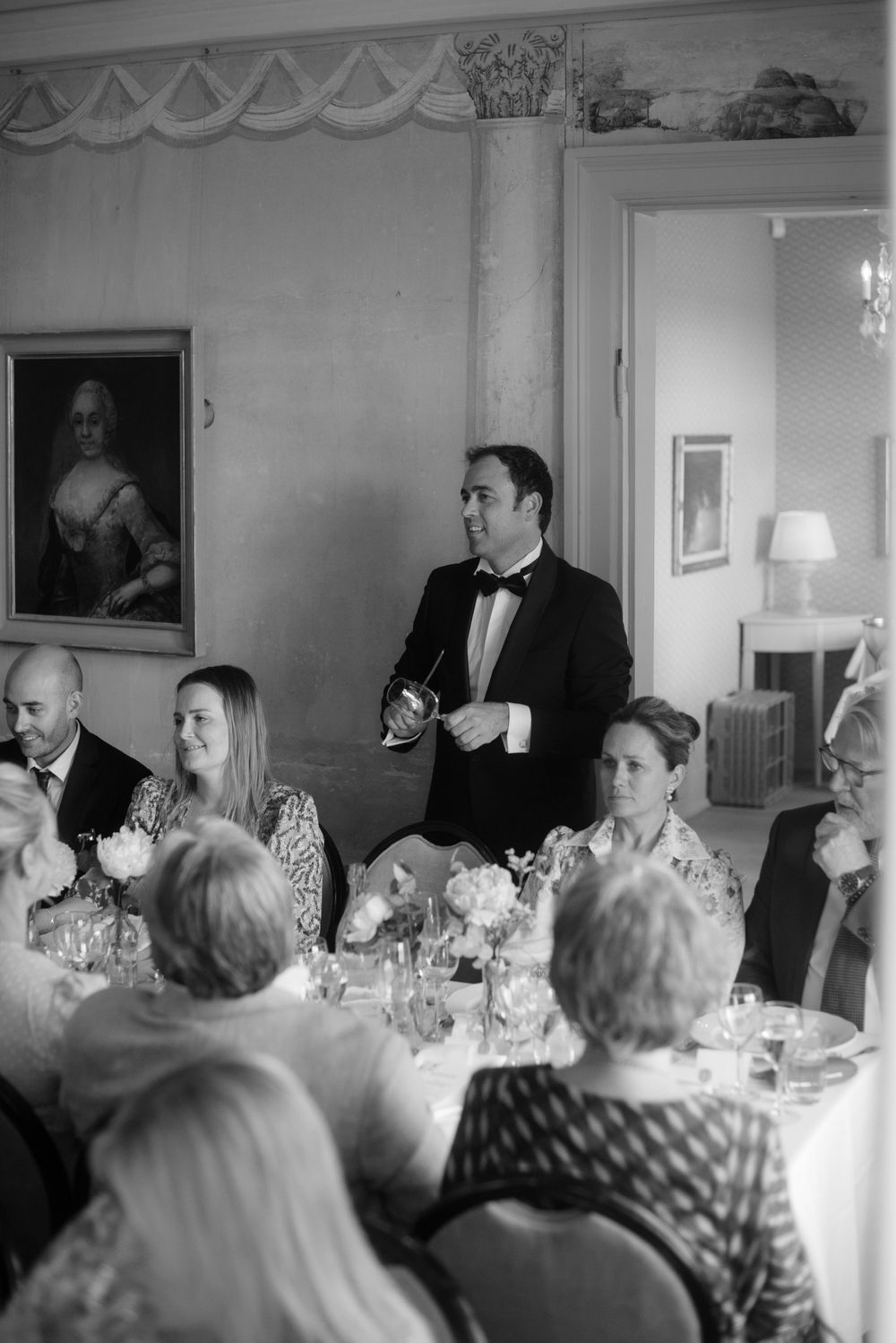 Black and white photo of formal dinner speeches in an elegant room with antique portrait.