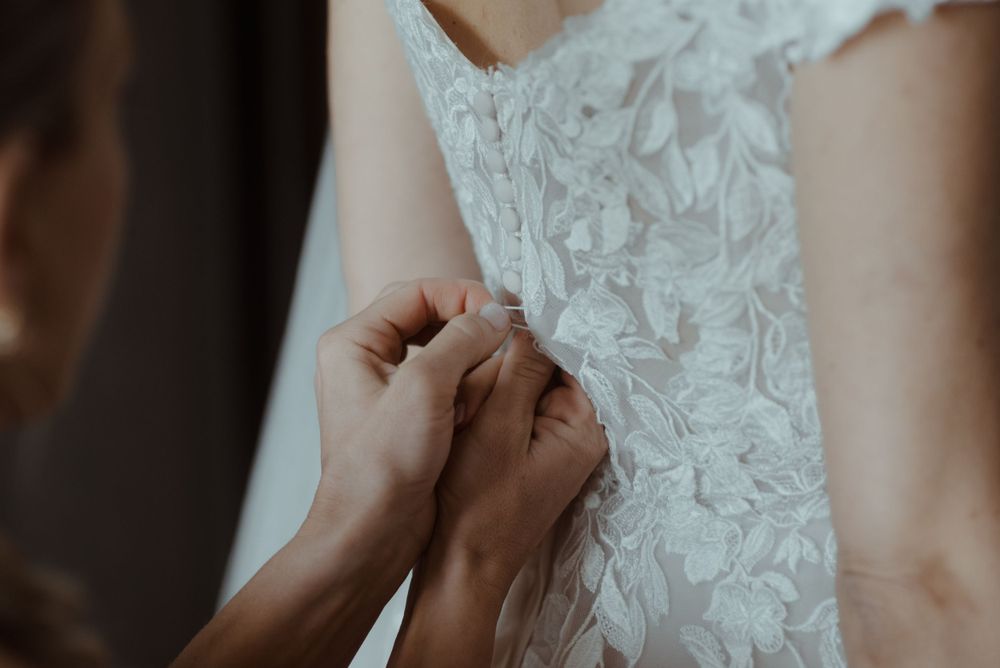 Close-up detail of hands adjusting intricate lace patterns on wedding dress.