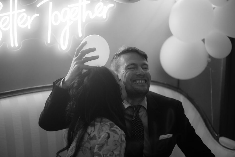 Black and white photo under neon lights with white balloons in background.