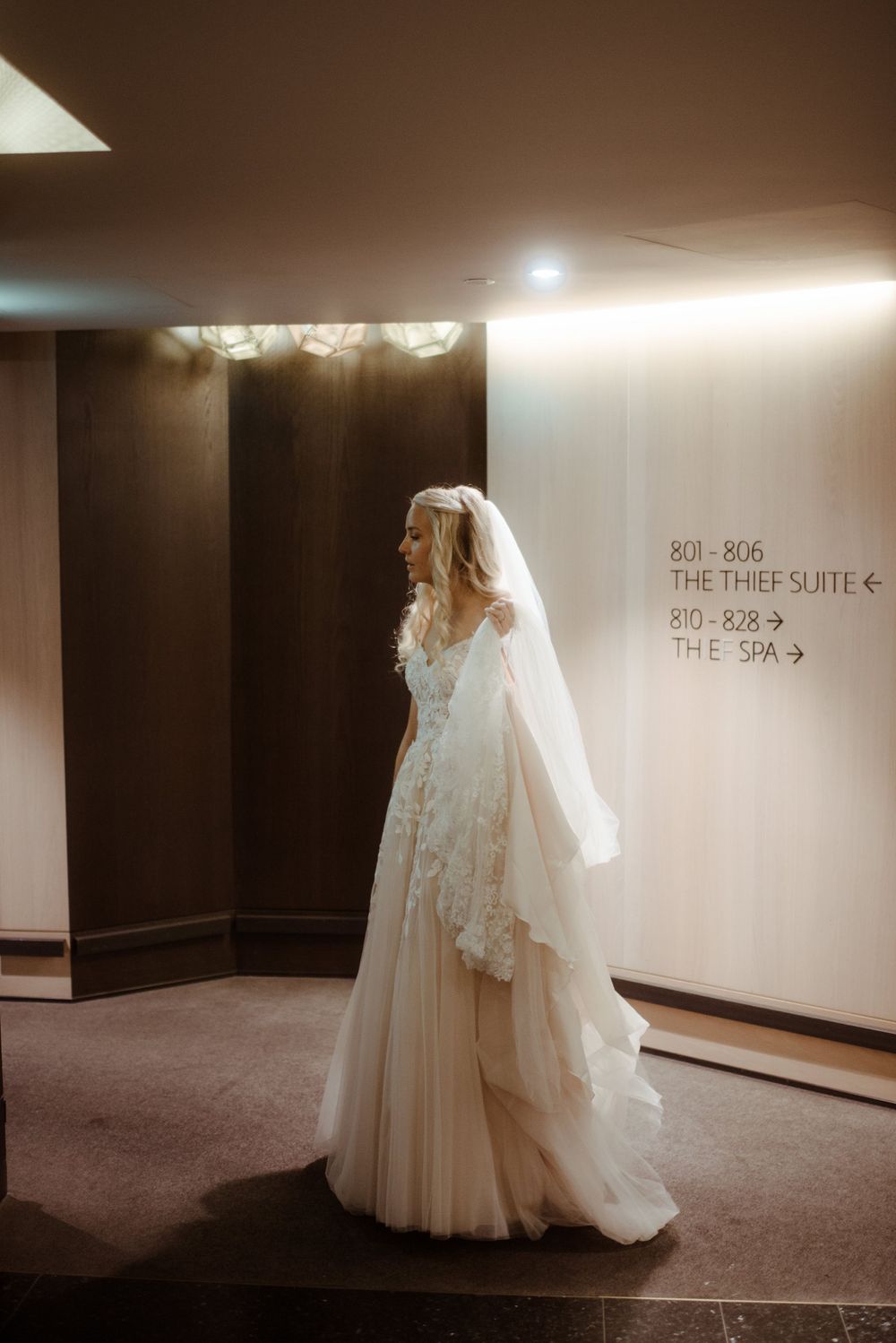A wedding dress displayed in a hotel hallway showcasing intricate lace details and flowing tulle.
