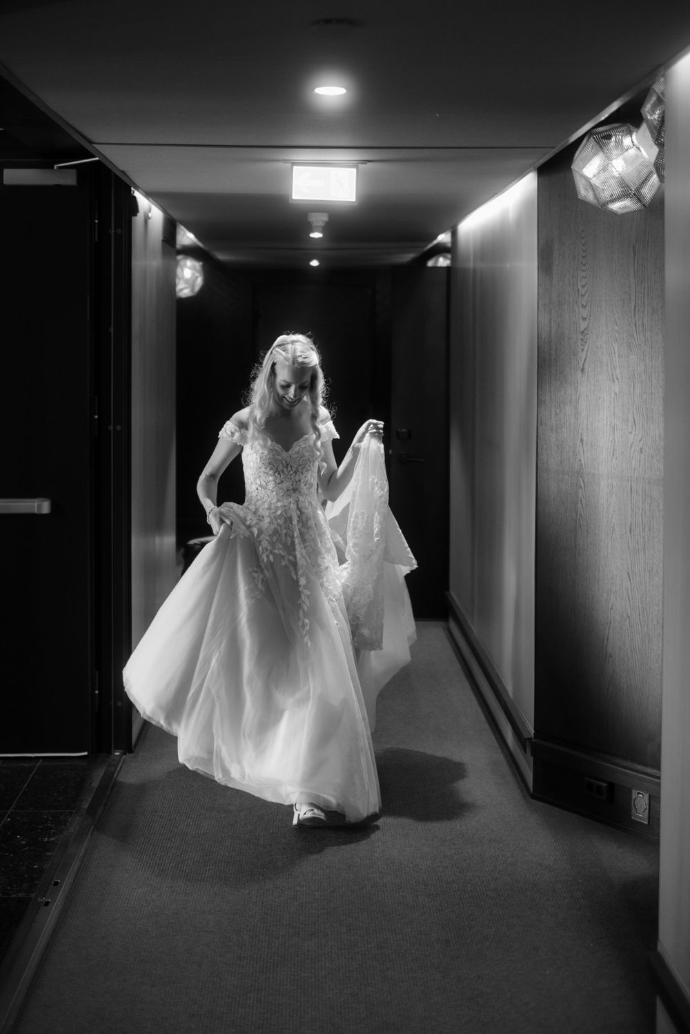 An elegant wedding dress flowing down a dimly lit hotel corridor.