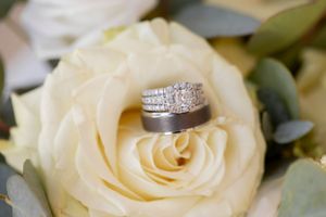 Wedding rings nestled in the petals of a cream-colored rose with greenery.