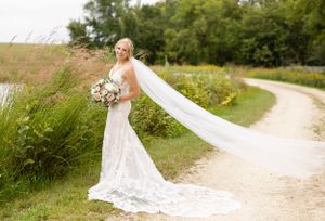 A bride poses on a winding path with her veil flowing dramatically in the breeze.