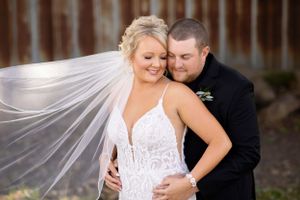 A romantic wedding portrait with flowing veil against rustic wooden backdrop.