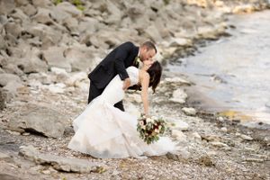 Wedding couple sharing intimate moment on rocky beach shore with bouquet.