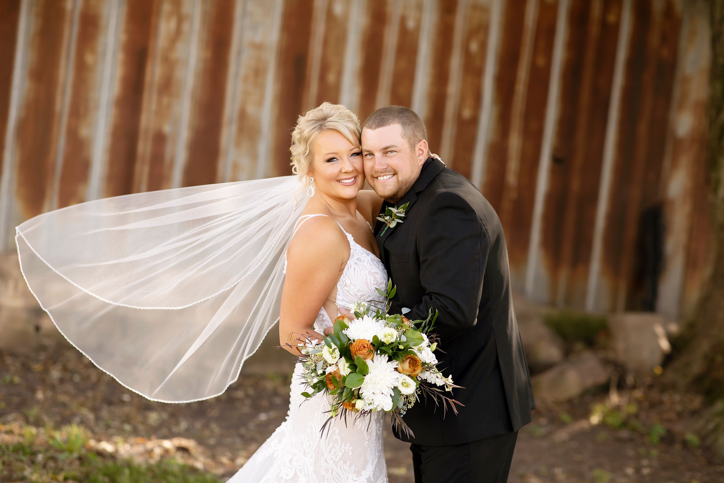 A joyful wedding couple shares a candid moment against rustic wooden backdrop.