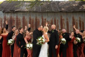 Wedding party celebrates with raised arms against rustic barn backdrop.