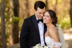 An elegant wedding couple shares an intimate moment outdoors in formal attire.