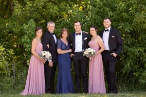 Wedding party in formal attire poses outdoors with bridesmaids in pink and navy gowns.