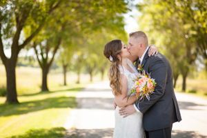Romantic wedding portrait on tree-lined path with couple embracing in sunlight.