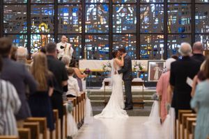 Church wedding ceremony with stained glass windows and guests in wooden pews.