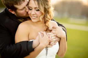 A romantic wedding couple embraces in soft golden light during their outdoor photo session.