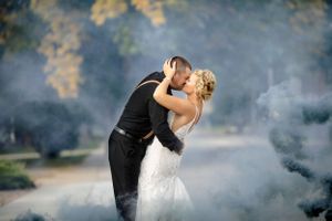 A wedding couple shares a romantic kiss surrounded by dramatic fog.