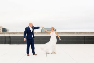 Wedding couple dances joyfully on rooftop with urban backdrop.