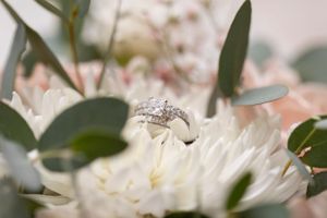 A diamond engagement ring nestled among white flower petals and green foliage.