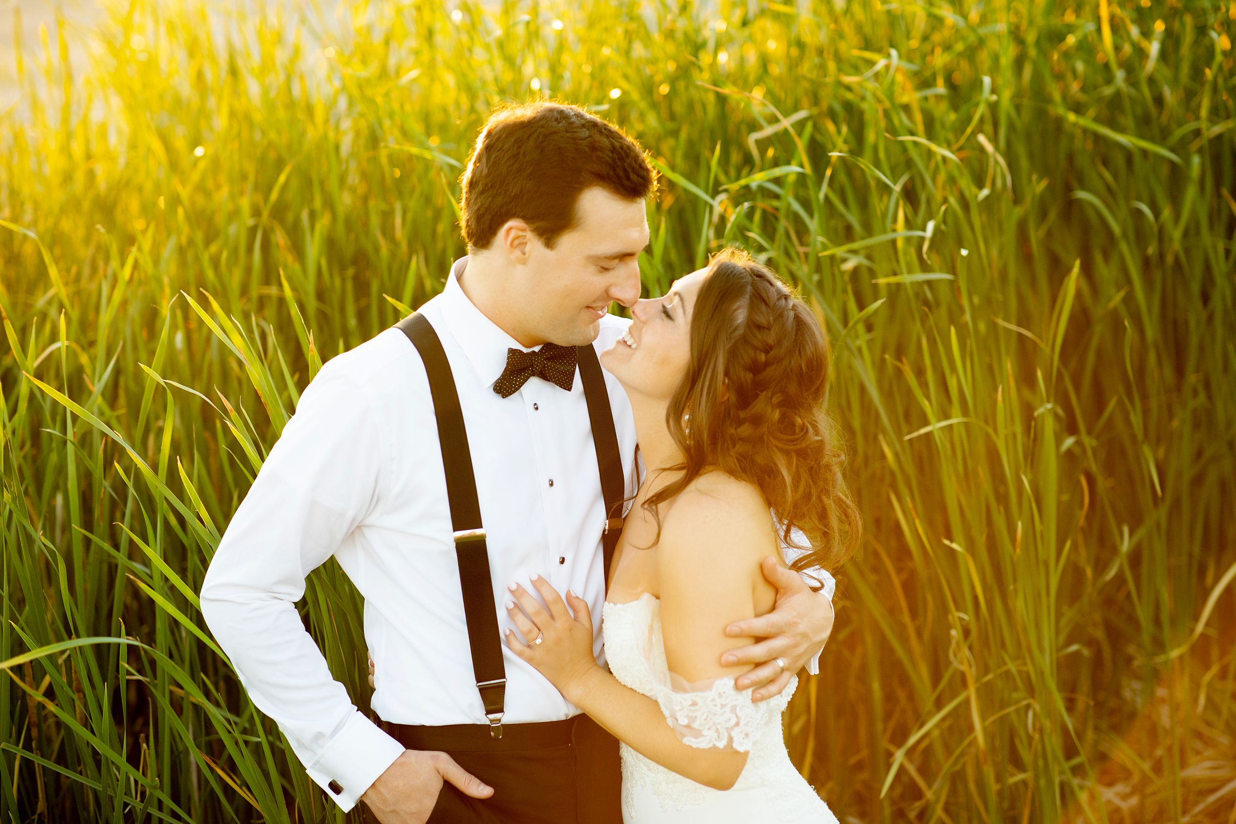 A romantic wedding couple embraces in a sunlit field of tall grass at golden hour.