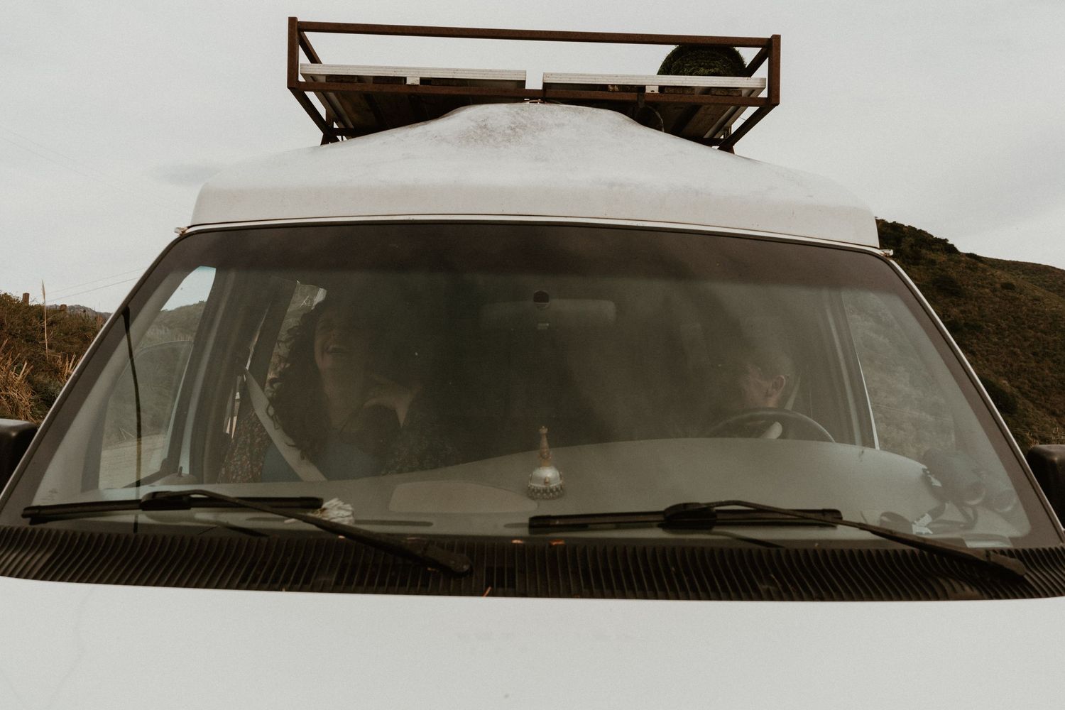 Close up view of a white car's windshield with a roof rack mounted on top against a dusky sky.