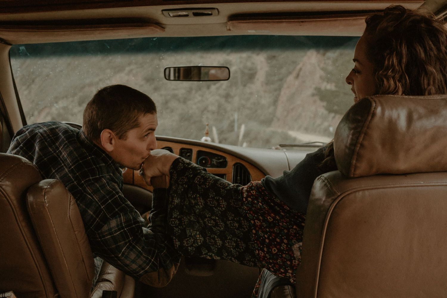 Two people sit in a vintage car with brown leather seats on a hazy autumn day.