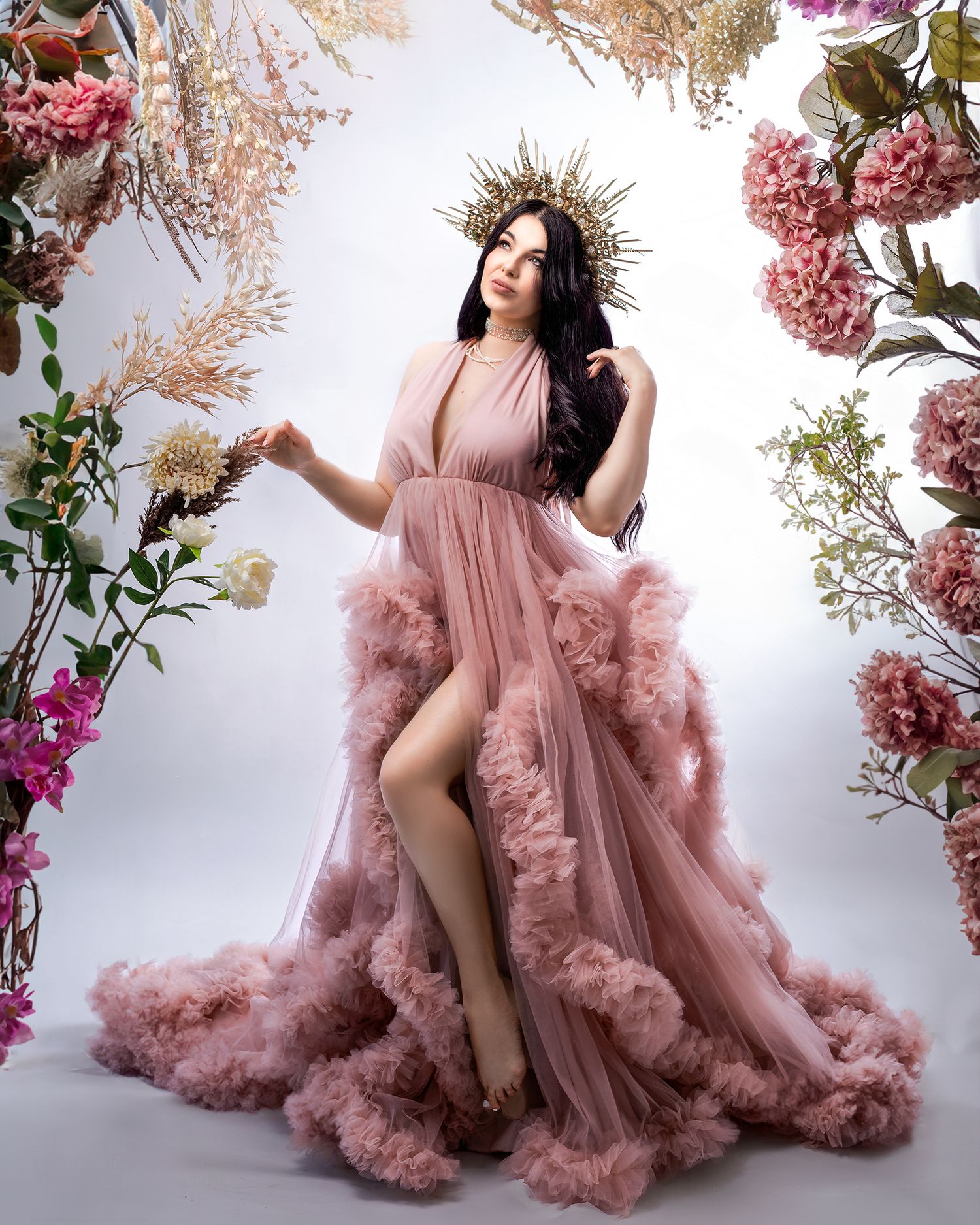 Woman in a pink gown, interacting with a prop like a floral archway in the studio.