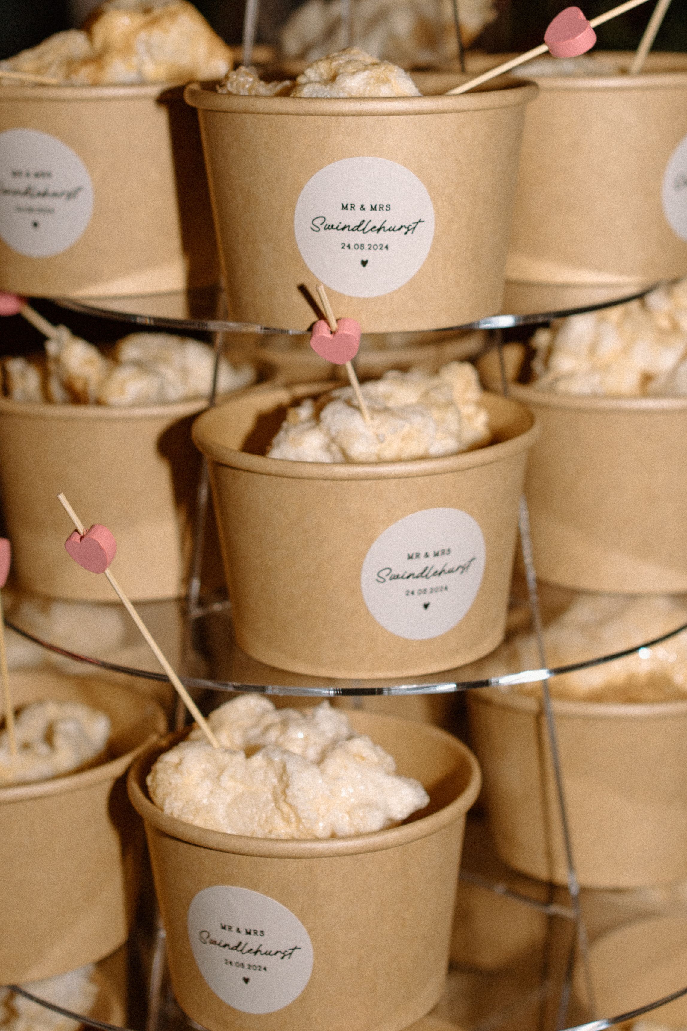 Kraft paper dessert cups filled with whipped cream and decorated with tiny pink heart toothpicks on a tiered display.