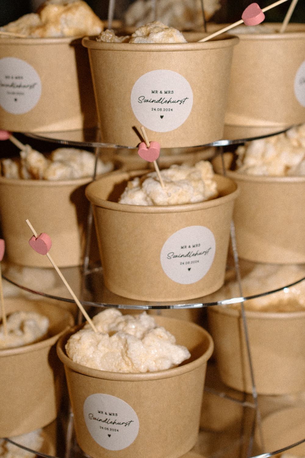 Kraft paper dessert cups filled with whipped cream and decorated with tiny pink heart toothpicks on a tiered display.
