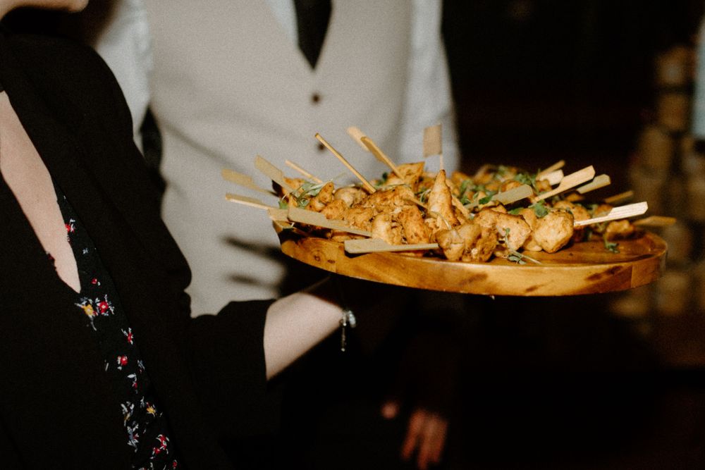 A server holds a wooden platter of appetizers with skewered hors d'oeuvres at an evening event.