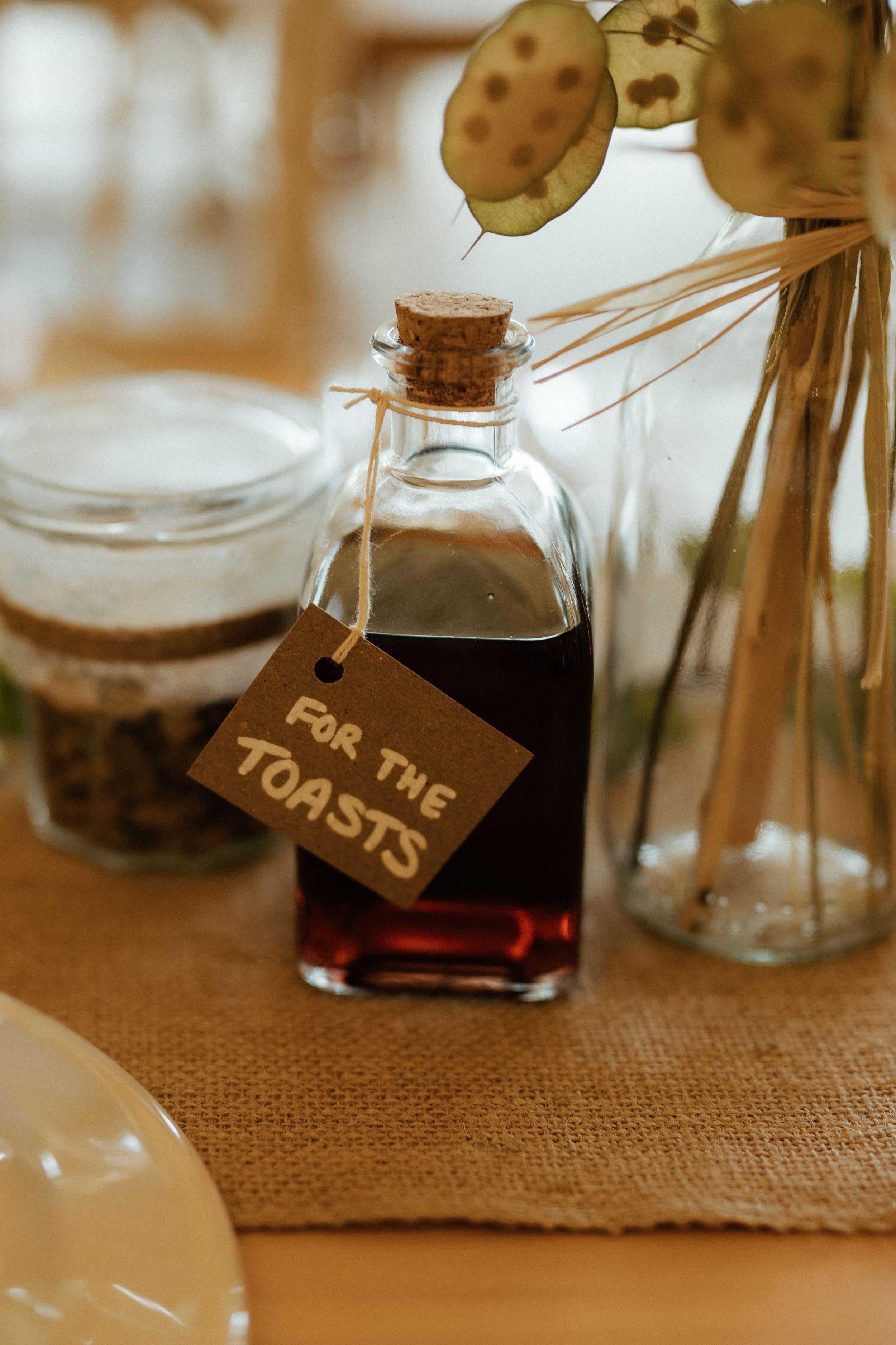 Small vintage glass bottles with wooden corks sit on a burlap cloth displaying rustic labels.