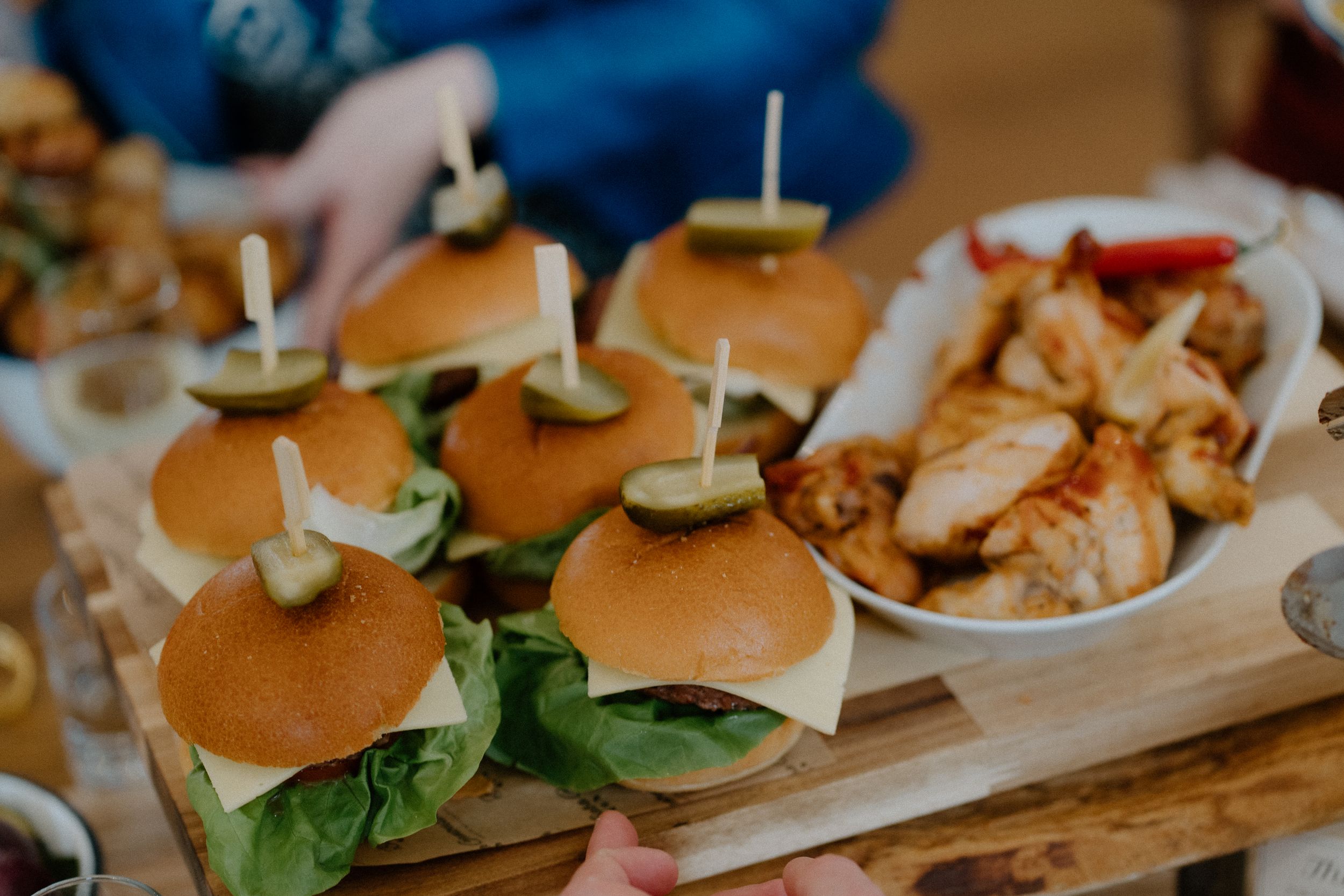 Gourmet sliders with fresh lettuce served on a wooden board alongside grilled chicken at a catered event.