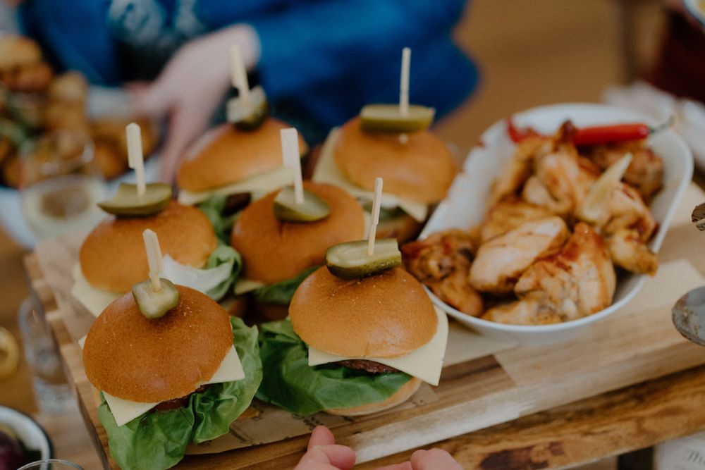 Gourmet sliders with fresh lettuce served on a wooden board alongside grilled chicken at a catered event.