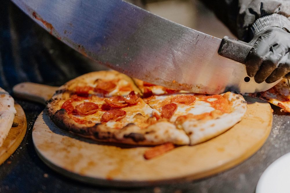 Pizza on a wooden cutting board topped with melted cheese and fresh basil captured in warm lighting.