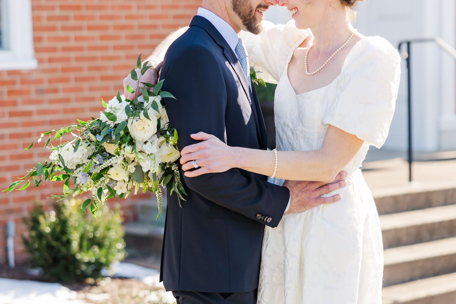 A tender moment between newlyweds embracing outdoors, the bride holding a lush green and white floral bouquet in Richmond, VA