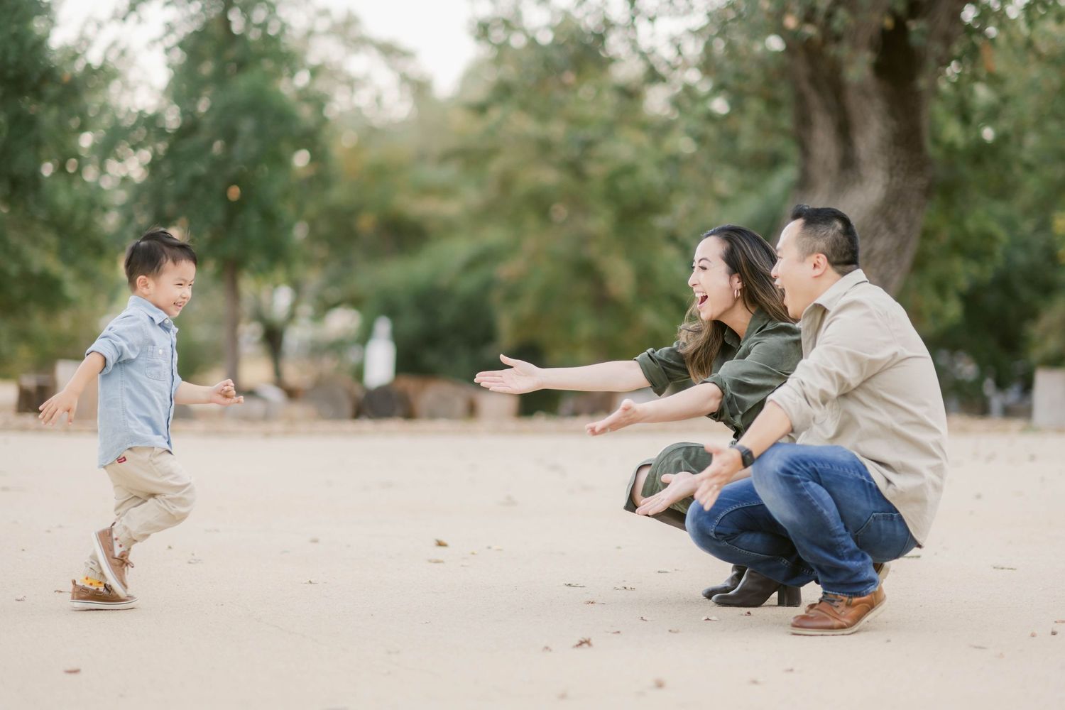 Family enjoying quality time together in a park on a sunny day, crouching and playing with child.