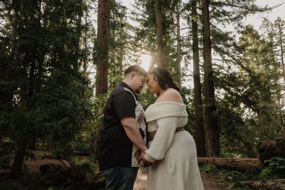 A loving couple shares a tender moment in a sunlit forest path while wearing casual winter attire.