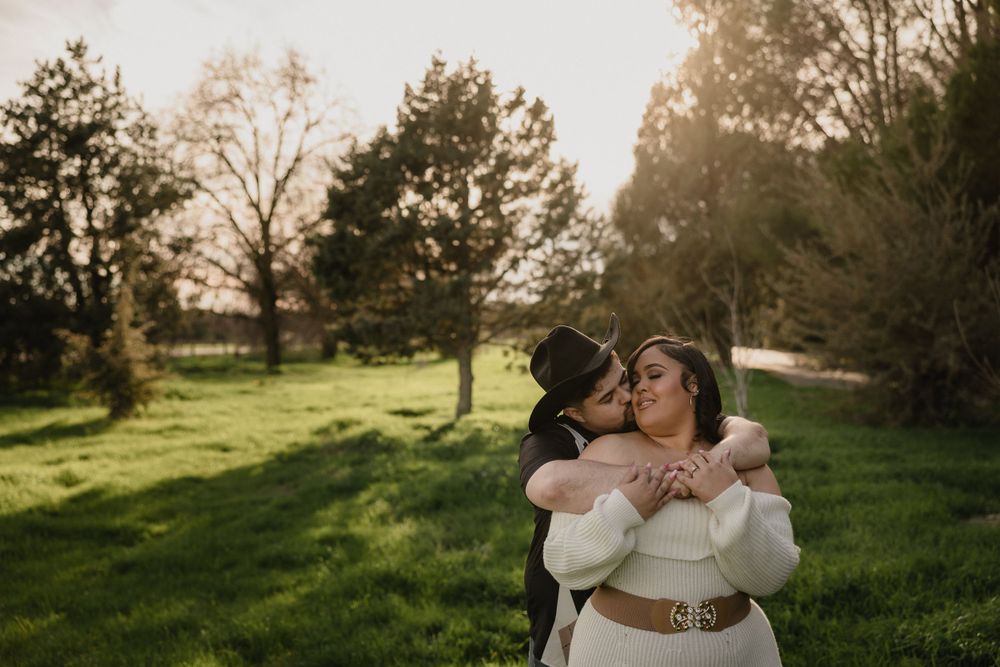 A tender embrace captured in a sunny meadow surrounded by trees at golden hour.