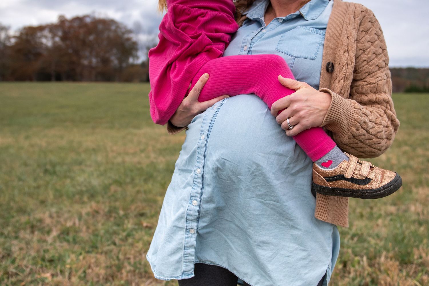 Close-up shots of someone wearing a light blue shirt and brown cardigan holding a bright pink item outdoors.