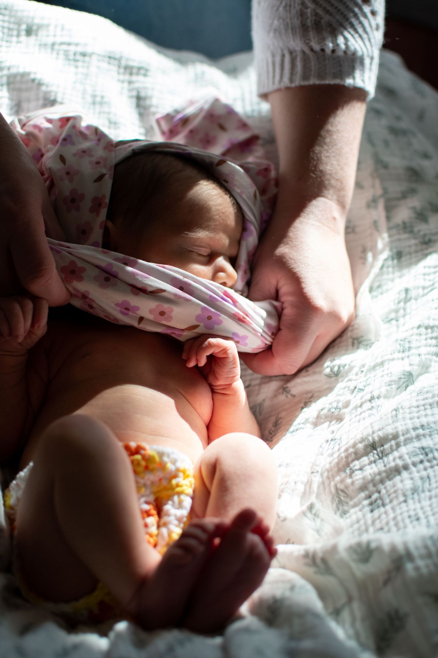 Gentle hands tend to a sleeping newborn baby swaddled in soft pink blankets on a white textured surface.