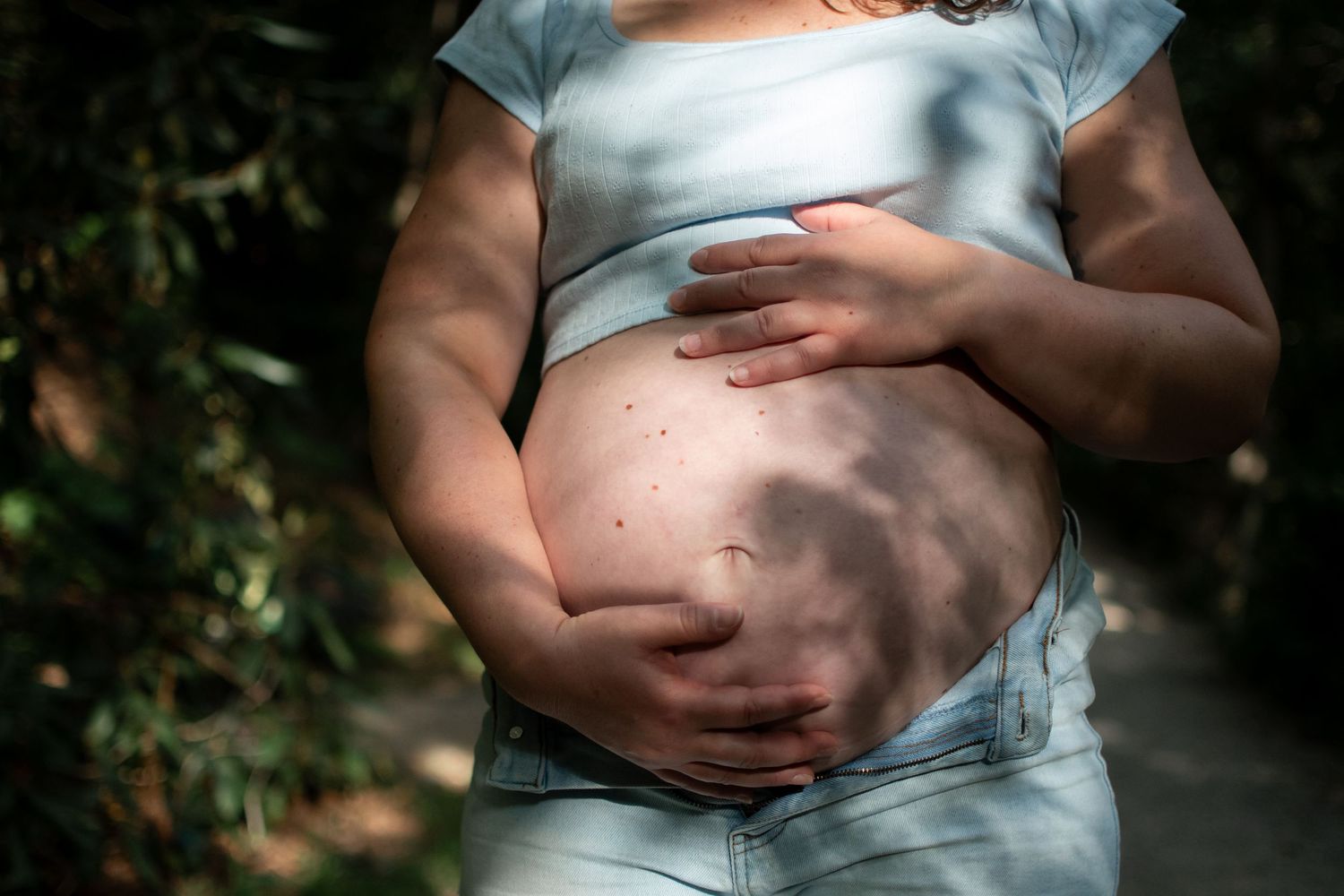 A series of maternity photos showing a pregnant belly in soft natural lighting against a dark background.