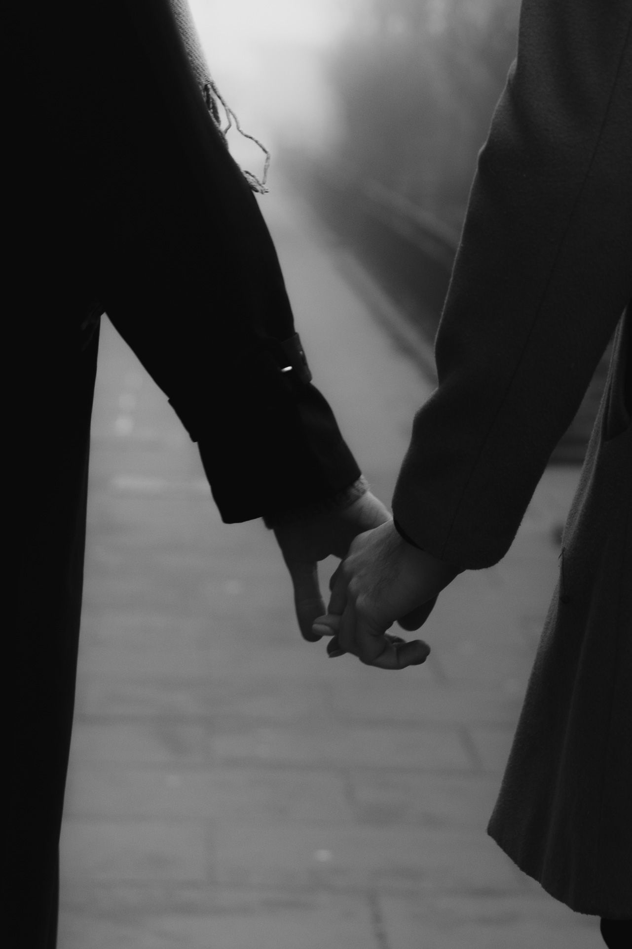 A black and white silhouette of two people holding hands together in an intimate moment.