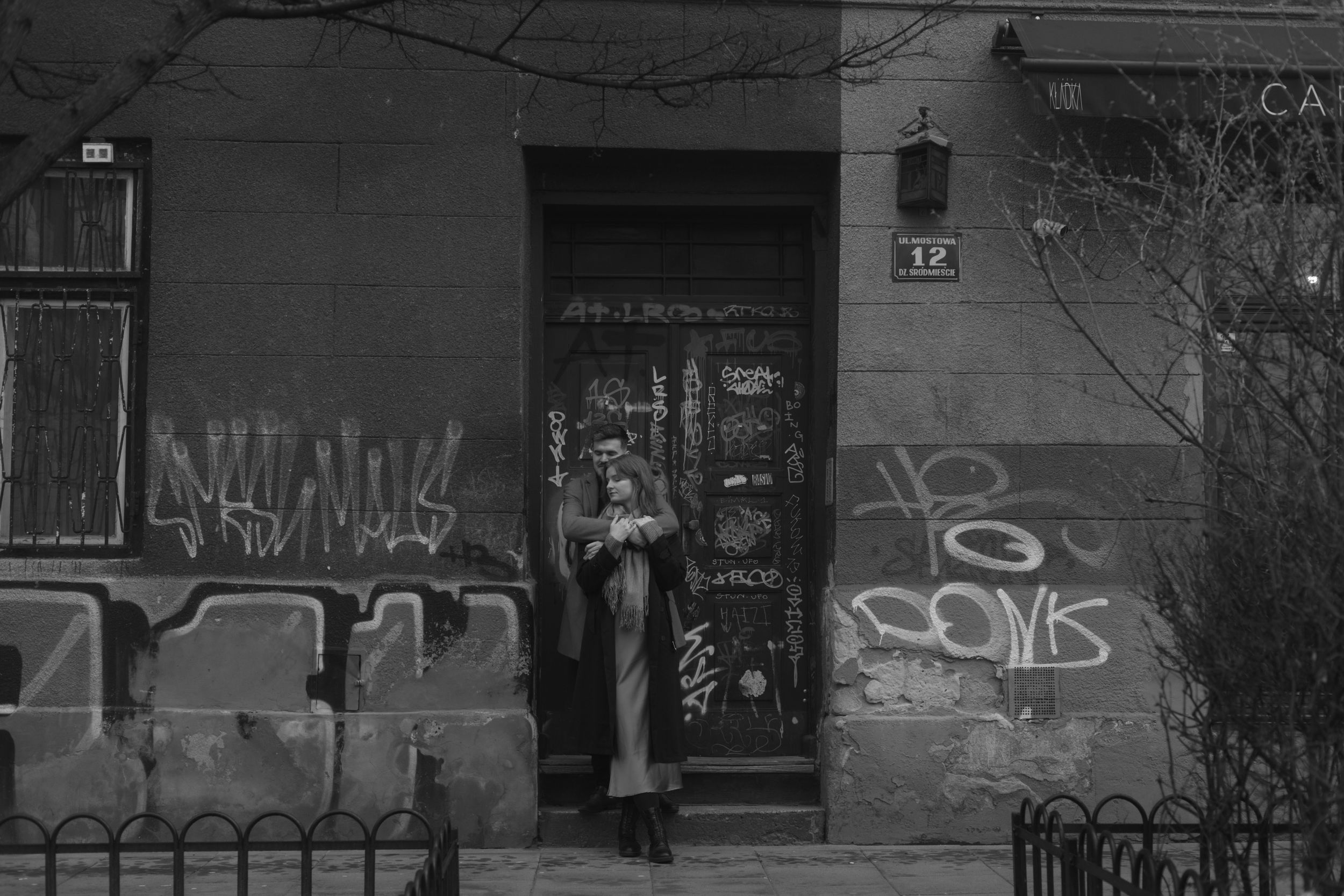 A person stands in front of a grungy doorway covered in graffiti on an urban building.