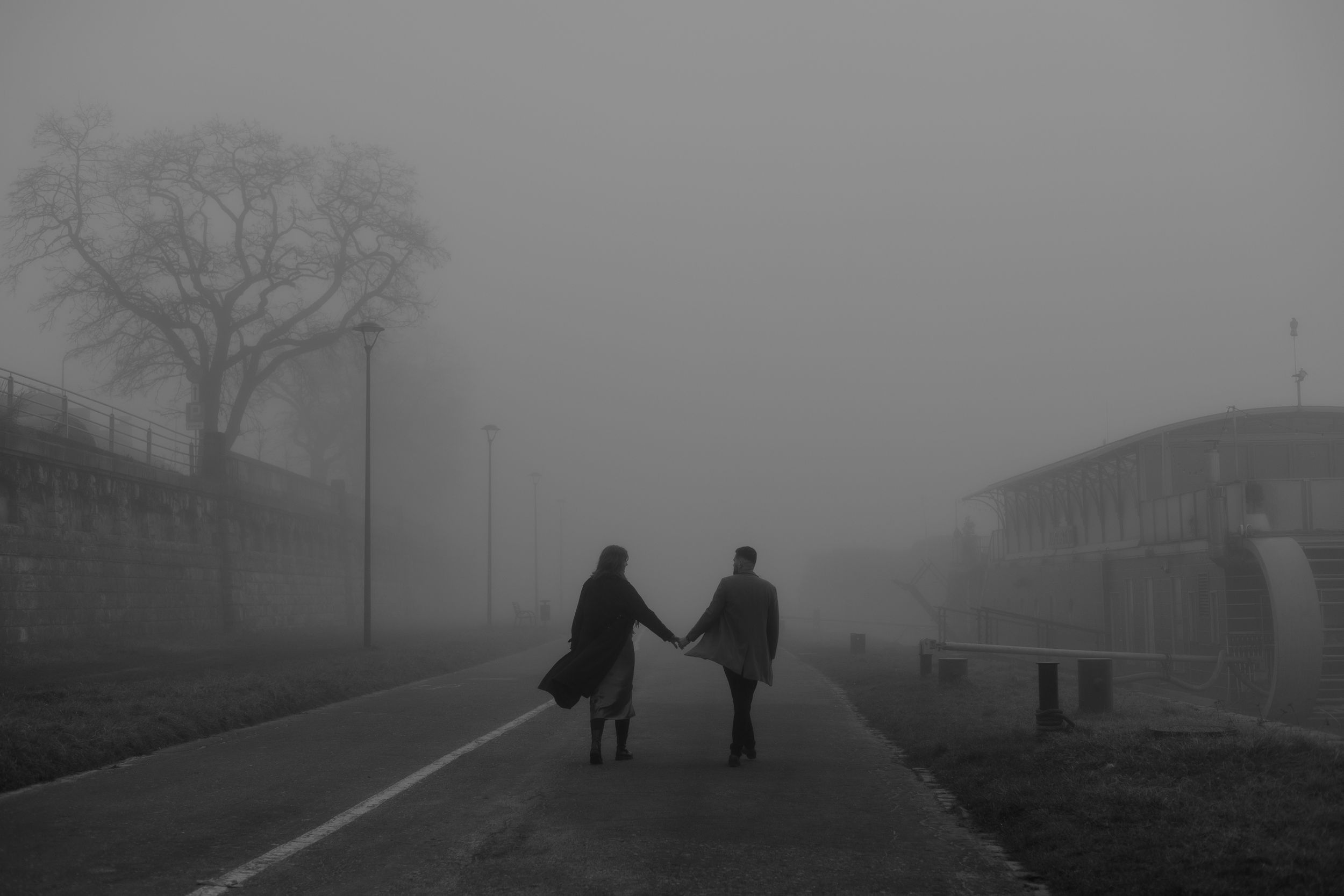 Two silhouetted figures hold hands while walking down a foggy street on a misty winter day.