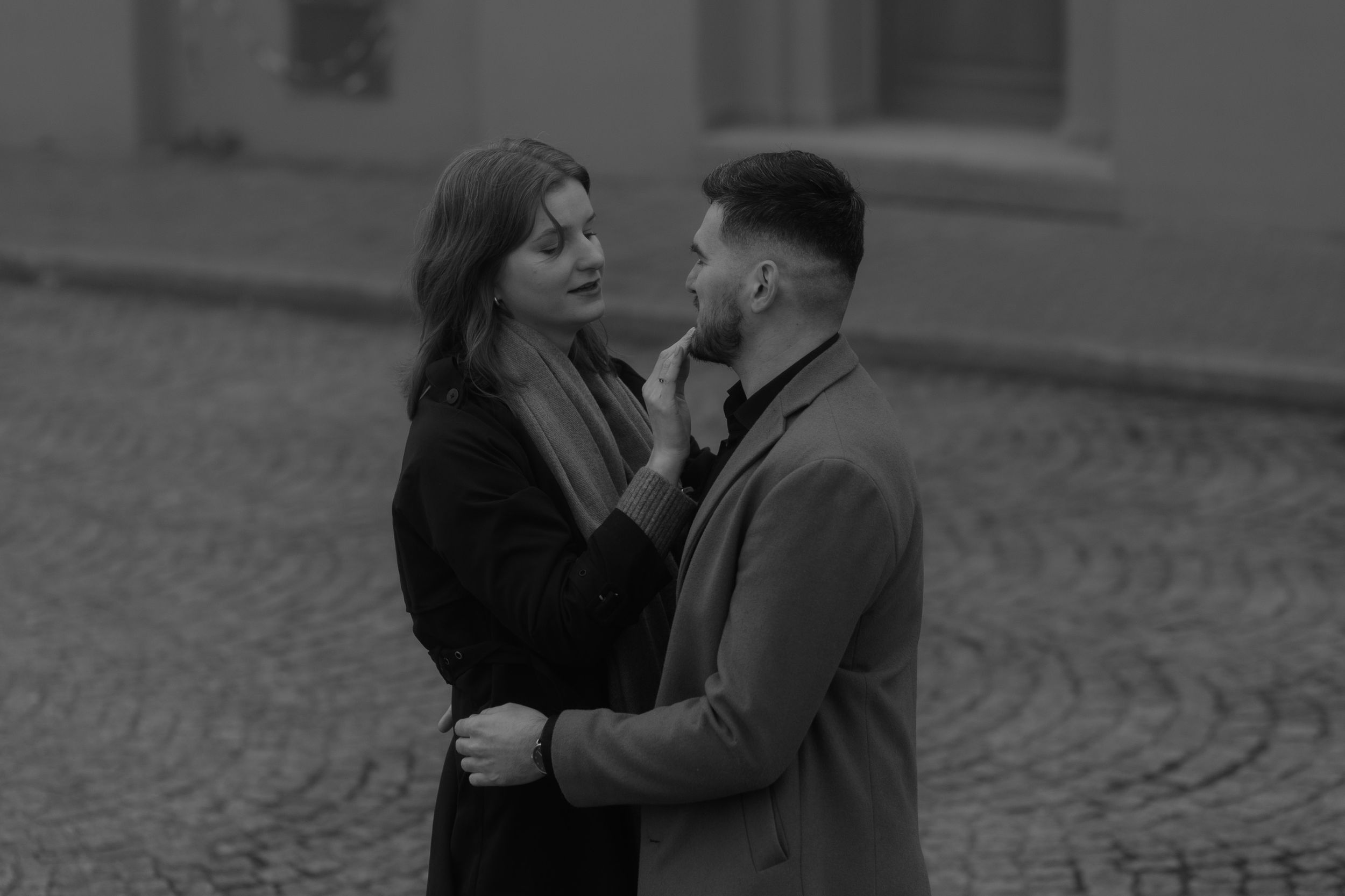 A romantic black and white moment between a couple embracing on a cobblestone street.
