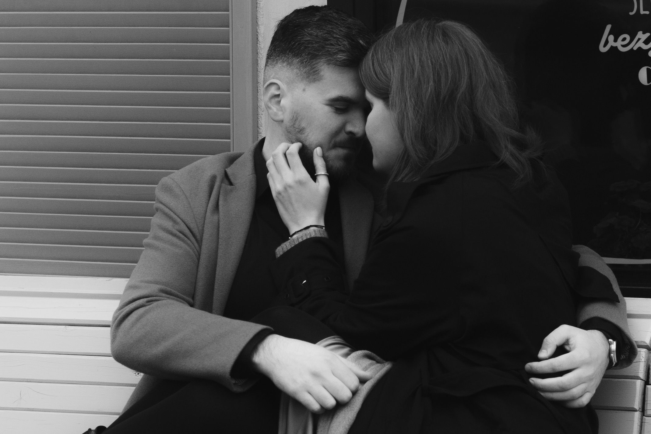 A romantic black and white photo of a couple sharing an intimate moment while sitting together on a bench.