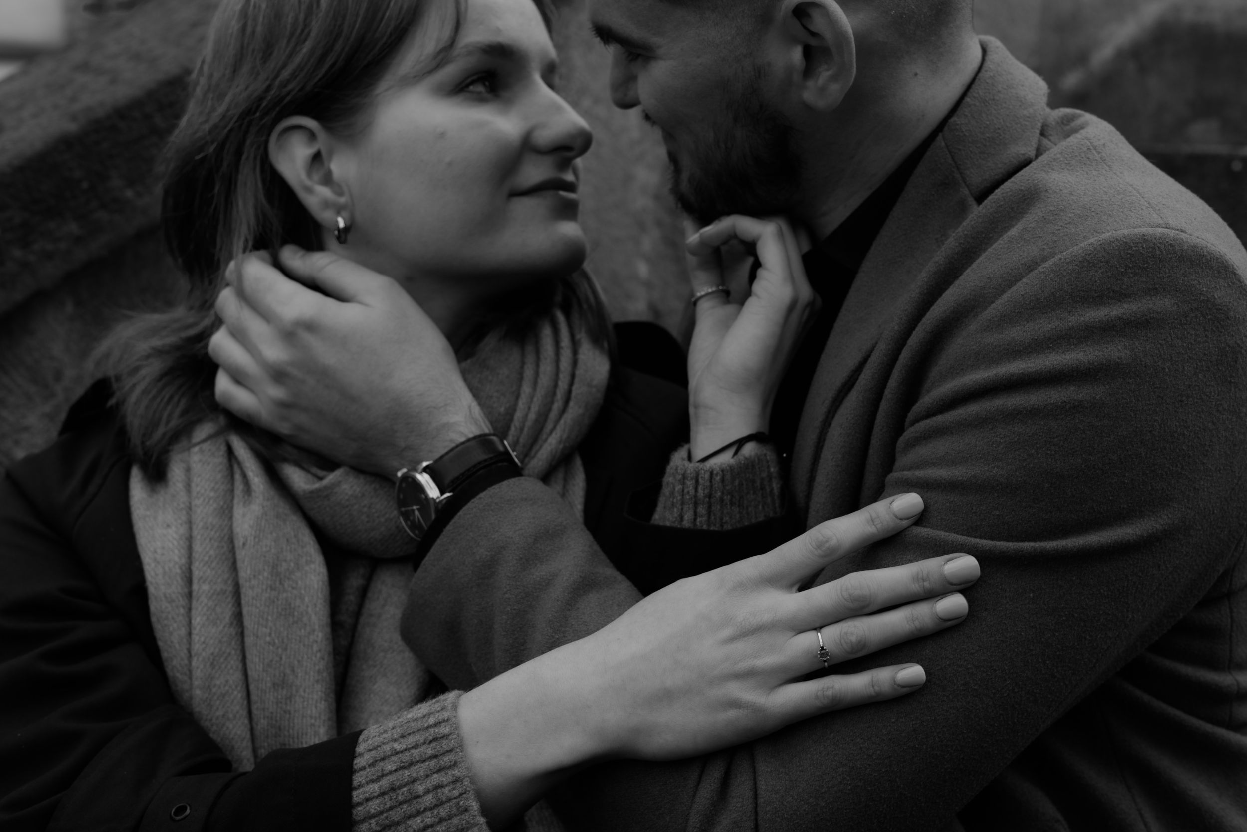 Black and white intimate photo of a couple embracing closely in winter clothing while looking into each others eyes.